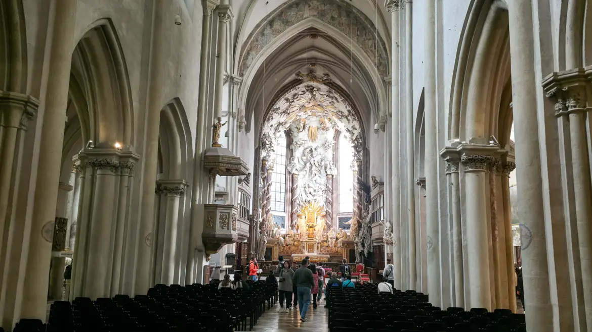 Interior of St. Michael’s Church in Vienna with Gothic vaulted ceilings, stone columns, and the dramatic high altar with the Fall of the Angels visible in the distance