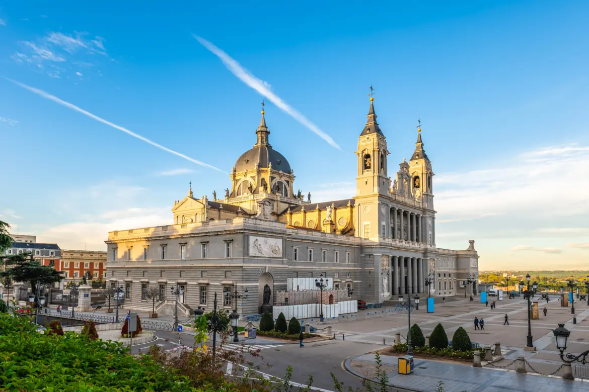 Almudena Cathedral in Madrid at golden hour, showing the full Neo-Classical facade with dome and twin towers against a blue sky