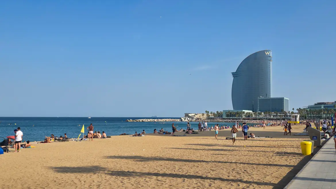 Barceloneta Beach at golden hour with the sail-shaped W Barcelona Hotel visible at the southern end of the coastline