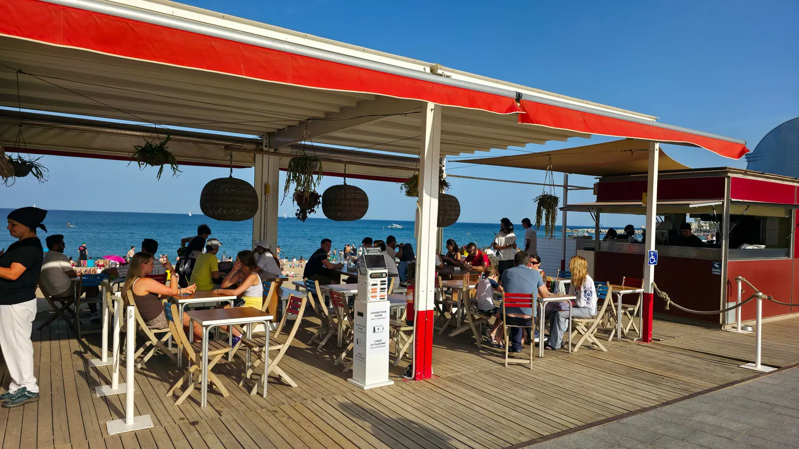 A beachside chiringuito at Barceloneta Beach in Barcelona, with terrace tables overlooking the Mediterranean where visitors enjoy fresh seafood, tapas, and chilled sangría