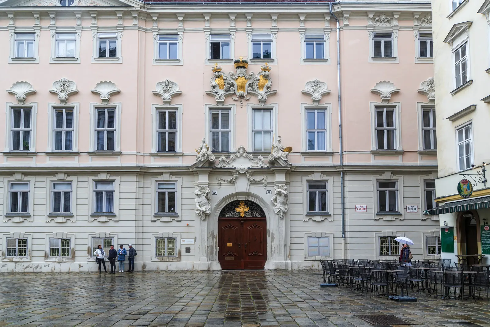 The Bohemian Court Chancellery at Judenplatz in Vienna, showcasing its elegant Baroque facade with gold ornamentation on a rainy day