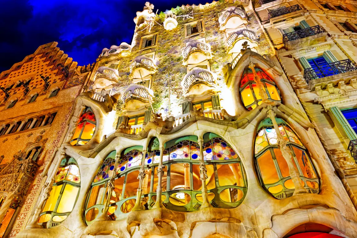 Casa Batlló at night on Passeig de Gràcia in Barcelona, with Gaudí's shimmering fish-scale façade illuminated against the dark sky — a UNESCO World Heritage masterpiece