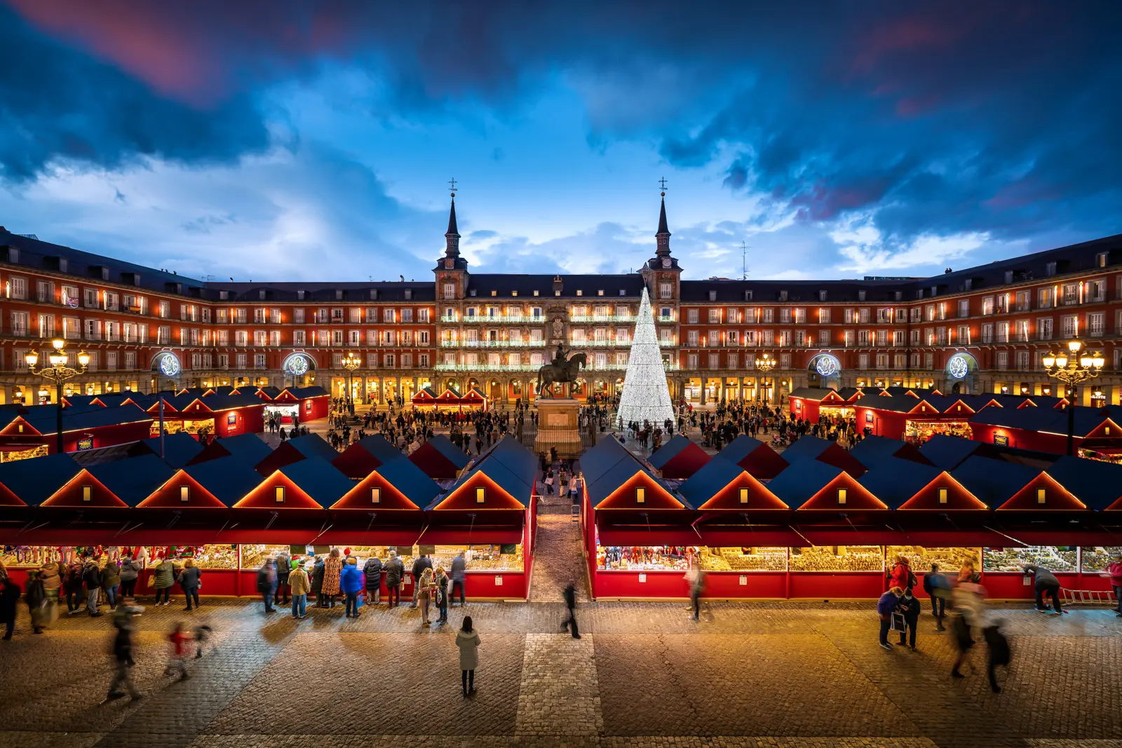 Christmas market at Plaza Mayor in Madrid, with wooden stalls, sparkling lights, and festive atmosphere under the evening sky