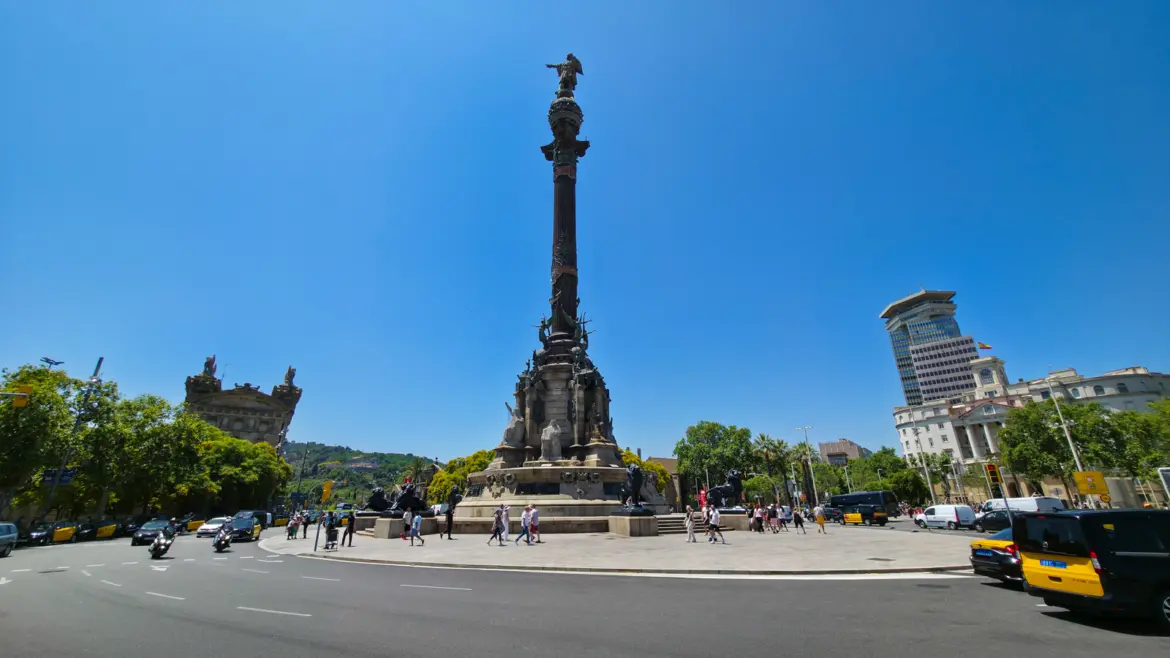 Wide view of the 60-metre Columbus Monument towering over Plaça del Portal de la Pau in Barcelona under bright midday sky