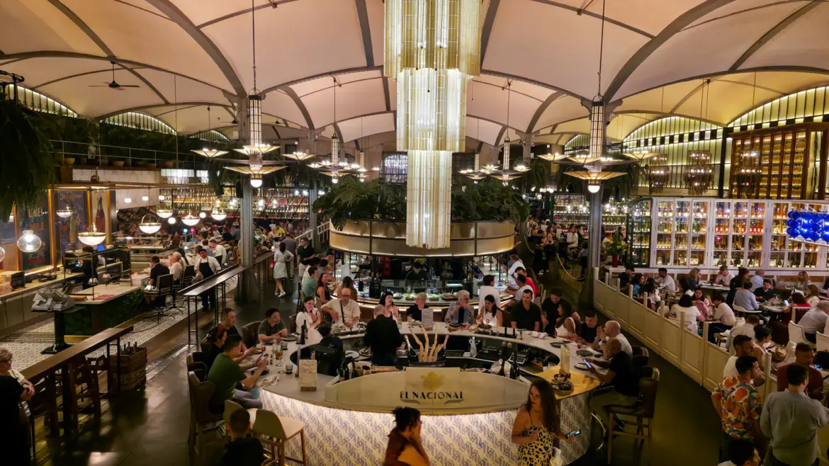 Wide elevated view of El Nacional Barcelona central atrium with the oval Cocktail Bar cascade chandelier vaulted ceiling and bustling diners