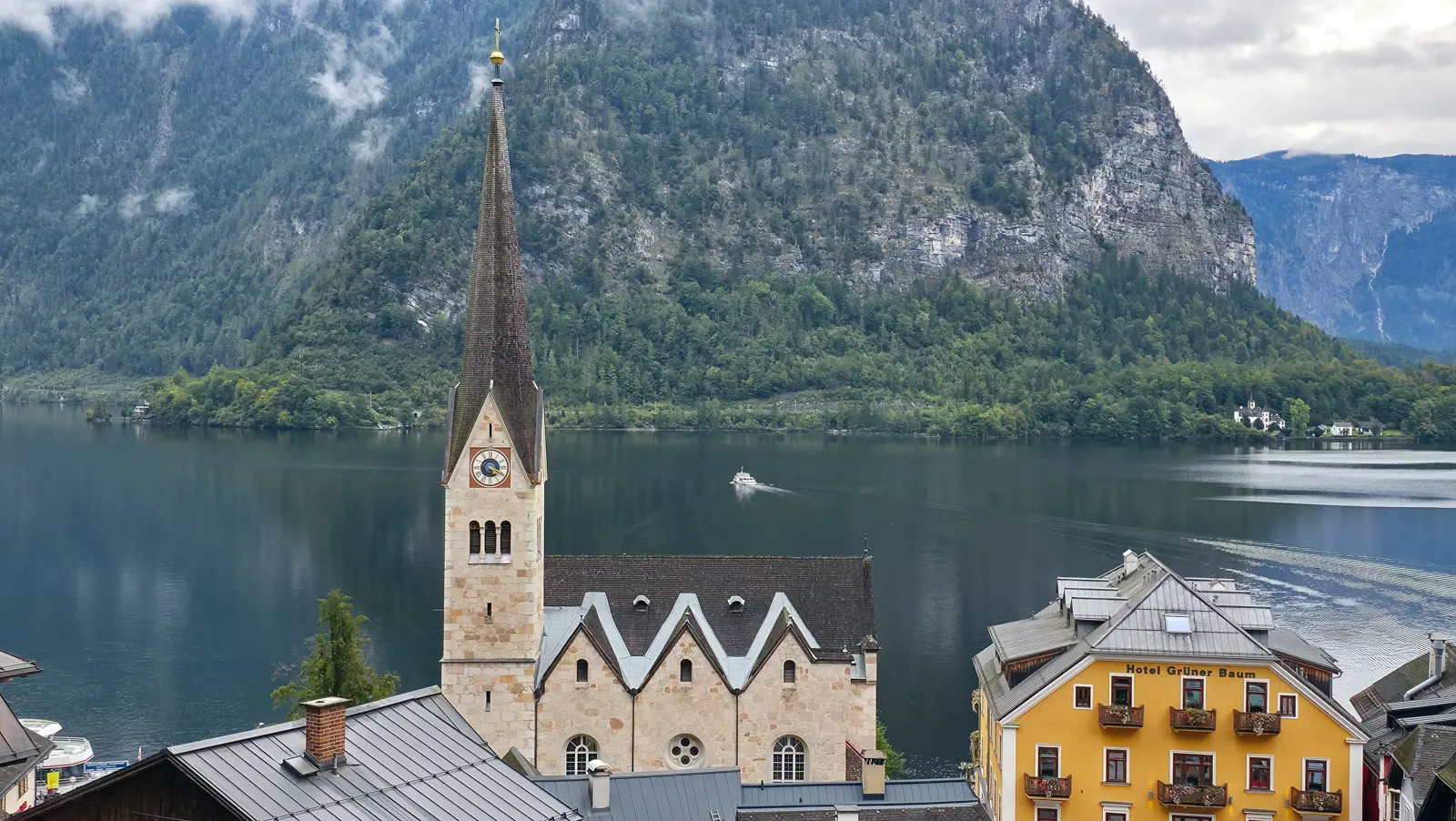 Neo-Gothic exterior of Evangelische Pfarrkirche Hallstatt with its slender bell tower and pointed spire, set against Lake Hallstatt and mountains