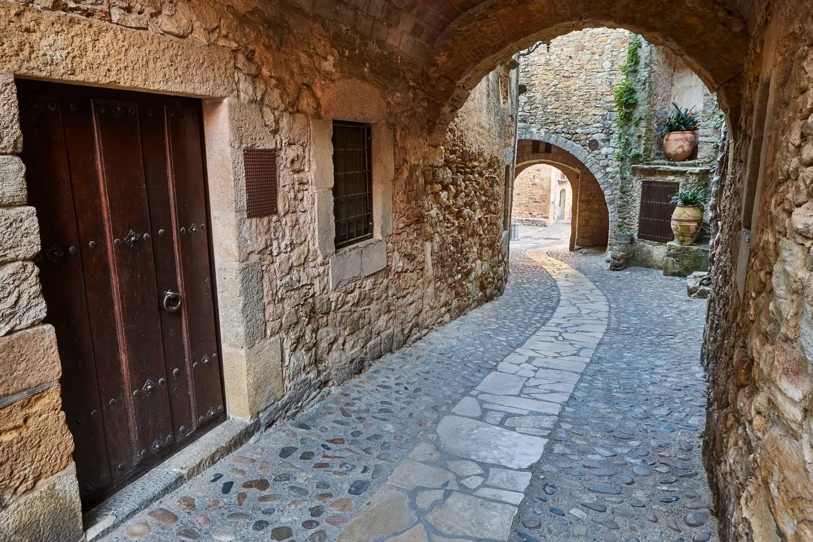 A narrow stone alley winding through Girona's atmospheric old town, where arched passageways and medieval walls served as filming locations for Game of Thrones