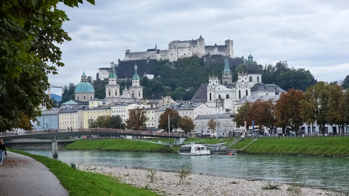 View of Hohensalzburg Fortress from the Salzach River with Salzburg Old Town and church spires along the waterfront