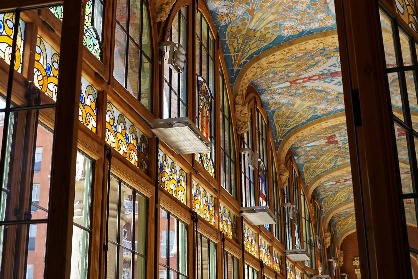 The stained glass and mosaic interior of Hospital de la Santa Creu i Sant Pau in Barcelona, where turquoise tiles, ceramic flowers, and colored light create a luminous palace-like atmosphere