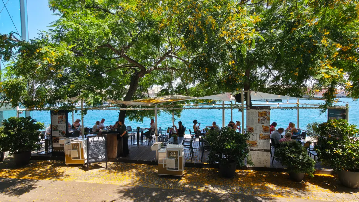 The upper terrace of Kurz & Gut Maremagnum in Barcelona's Port Vell, with sun-washed wood, parasols, and harbour views