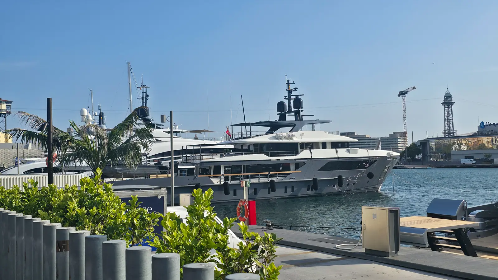 Superyachts moored at Marina Port Vell in Barcelona in bright midday sun with the red Torre Jaume I aerial tramway tower visible behind