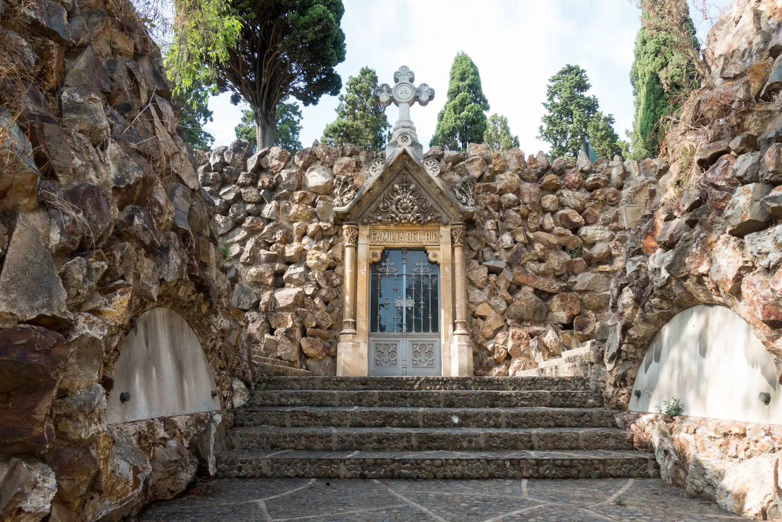 The terraced paths of Montjuïc Cemetery in Barcelona, with marble tombs and sculptures cascading down the hillside toward the Mediterranean below