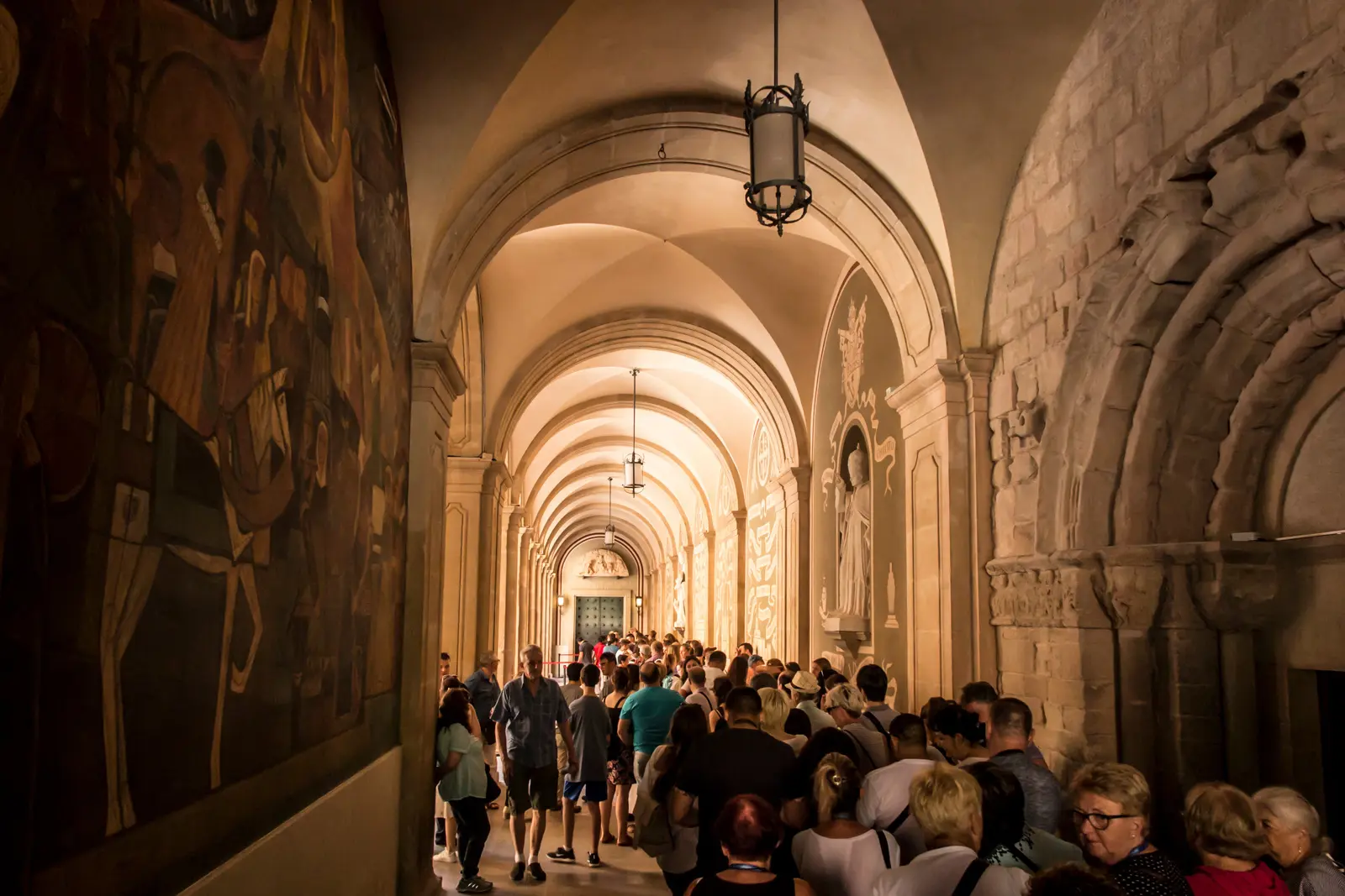 Visitors queuing inside the Basilica of Montserrat along the raised walkway that leads behind the altar to the Black Madonna's chamber, lined with votive offerings from centuries of pilgrims