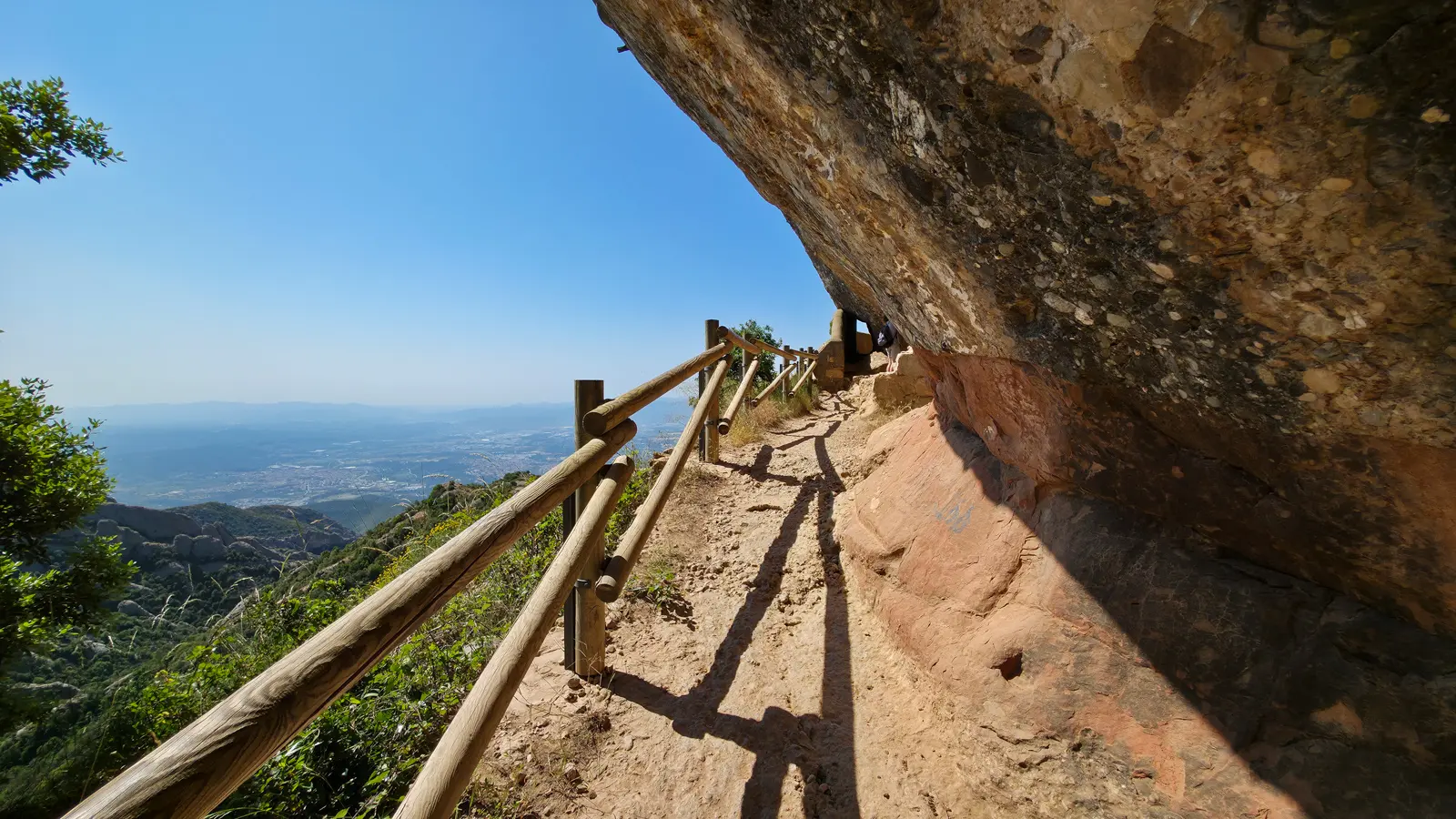 Hiking trail along Montserrat's upper ridge, winding past enormous rounded rock towers carved over millions of years, with pine-filled ravines and open ridgelines stretching toward the Catalan horizon