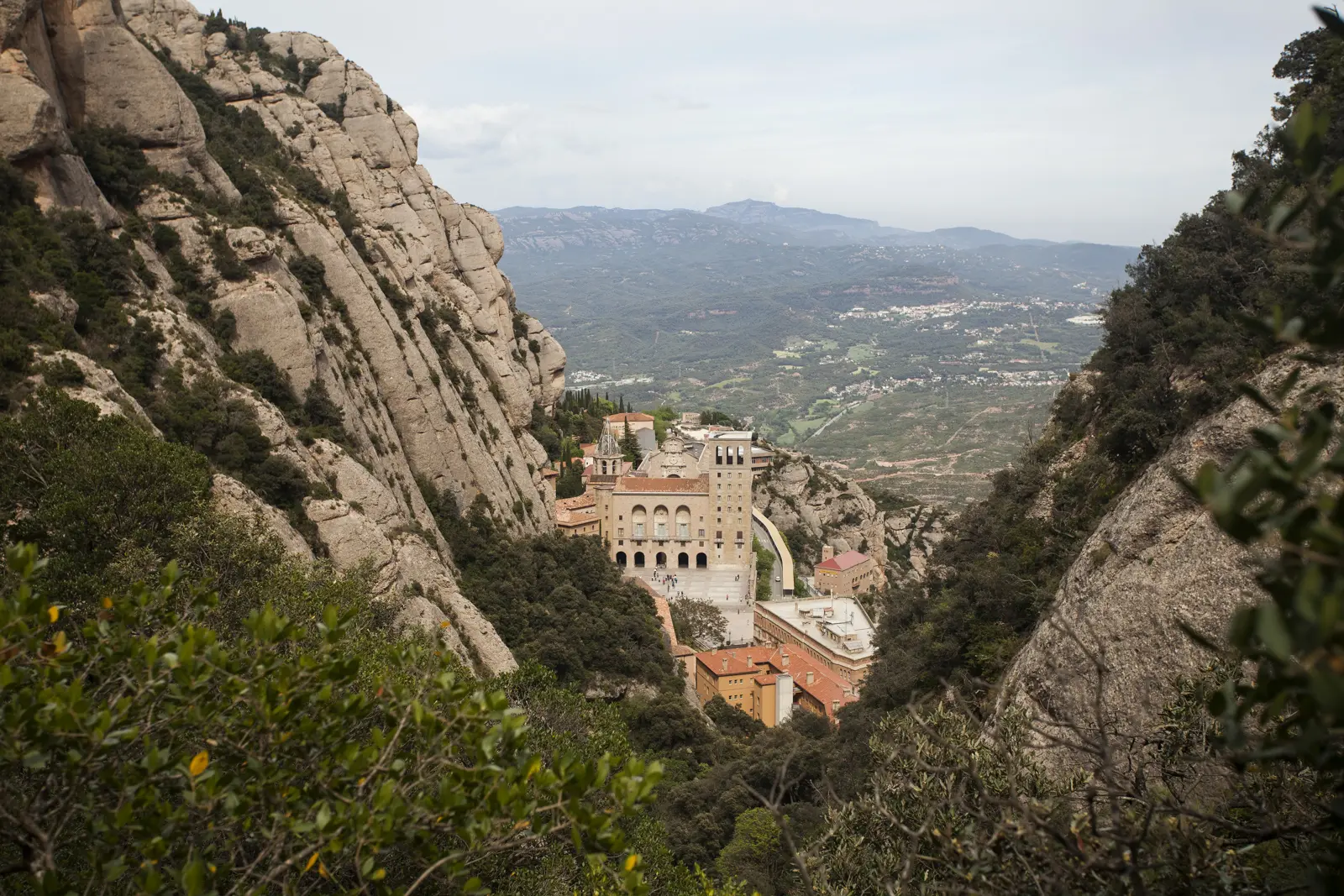 The abbey of Santa Maria de Montserrat shimmering golden in the afternoon light, viewed from a quiet personal viewpoint high above, with clear sky arching endlessly overhead