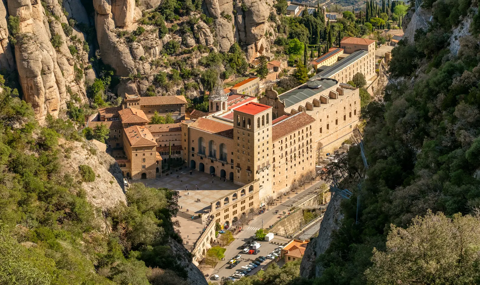 The monastery of Montserrat from the ascending Sant Joan funicular, shrinking into a cluster of ochre rooftops with its courtyard and basilica delicate against the serrated jagged cliffs