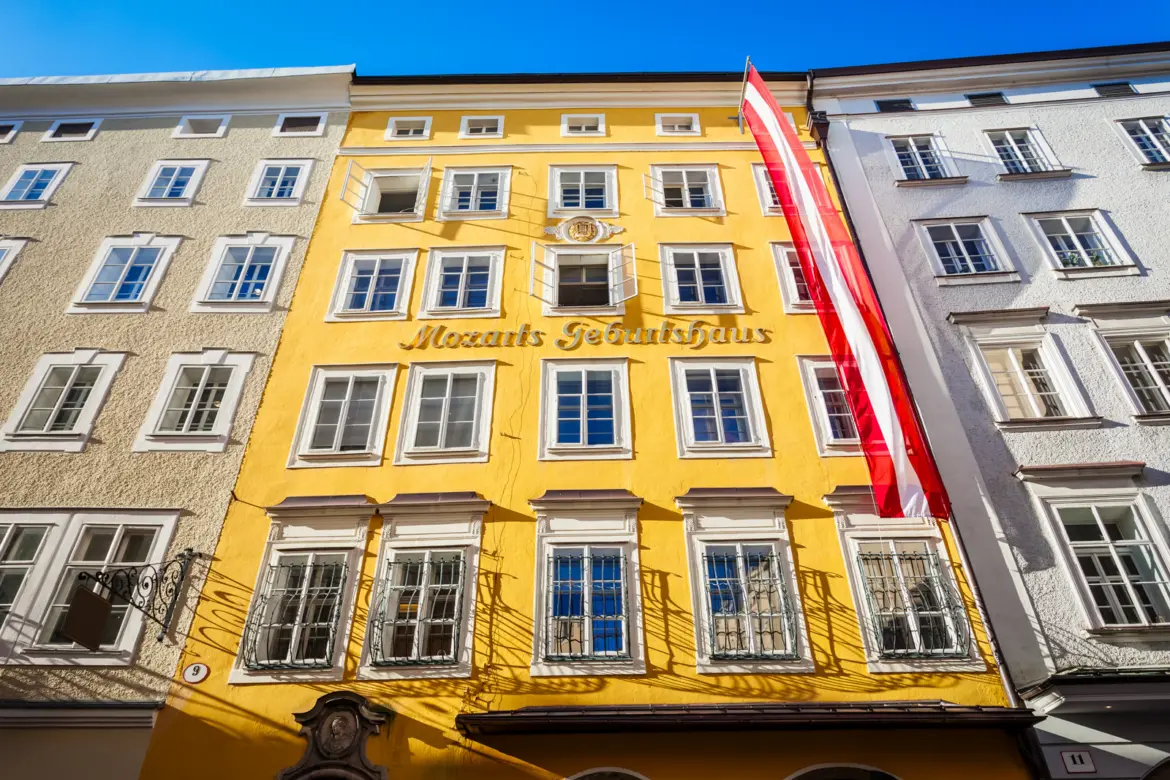 Bright yellow facade of Mozart's Birthplace on Getreidegasse with Mozarts Geburtshaus gold lettering and Austrian flag in Salzburg