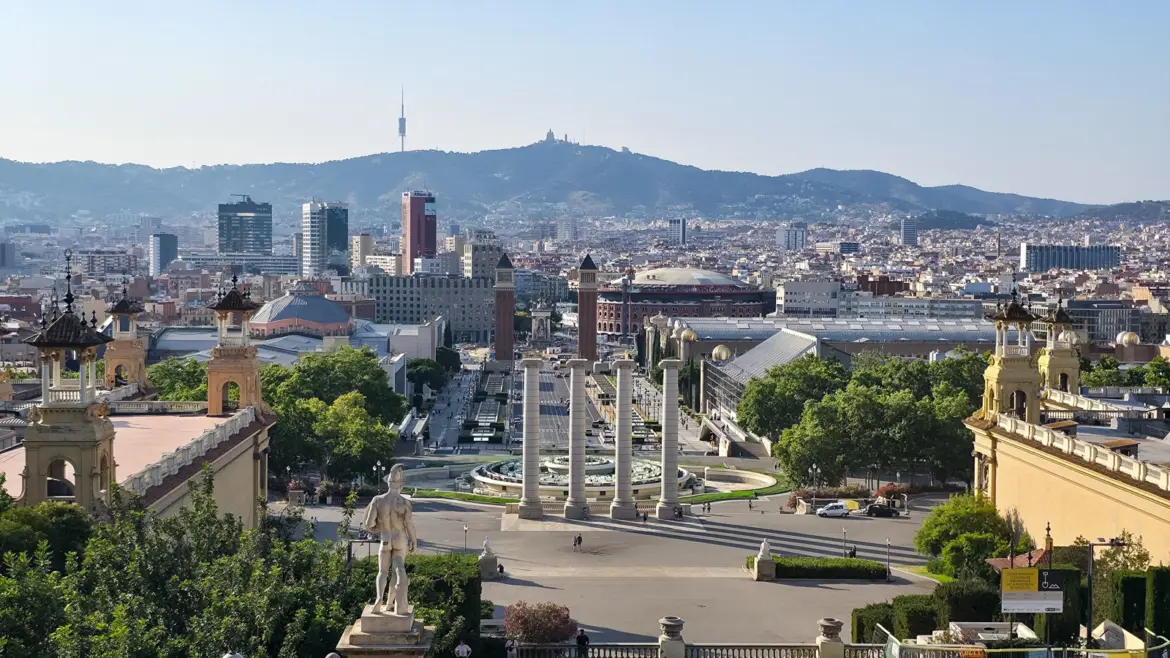 Panoramic view from Palau Nacional looking down Avinguda de la Reina Maria Cristina toward Plaça d'Espanya, showing the Four Columns, Venetian Towers, Arenas de Barcelona, and Tibidabo mountain in the distance, Barcelona, Spain