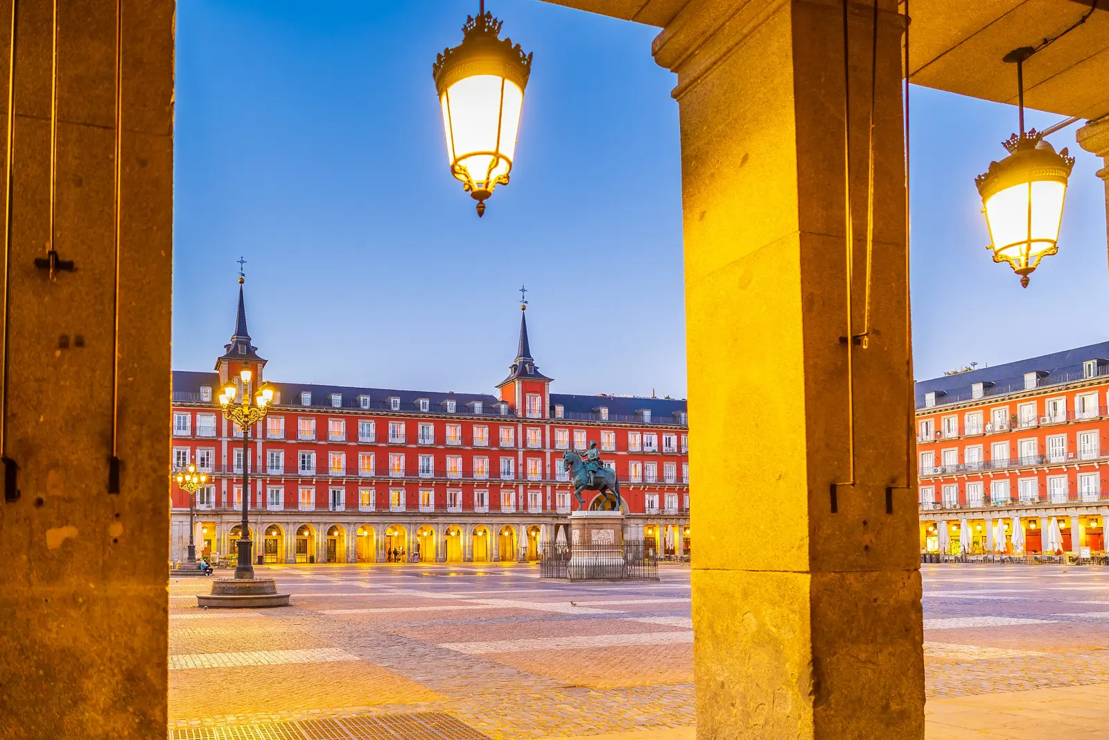 Plaza Mayor in Madrid at sunset, with golden light reflecting against the terracotta facades and warm shadows stretching across the cobblestones