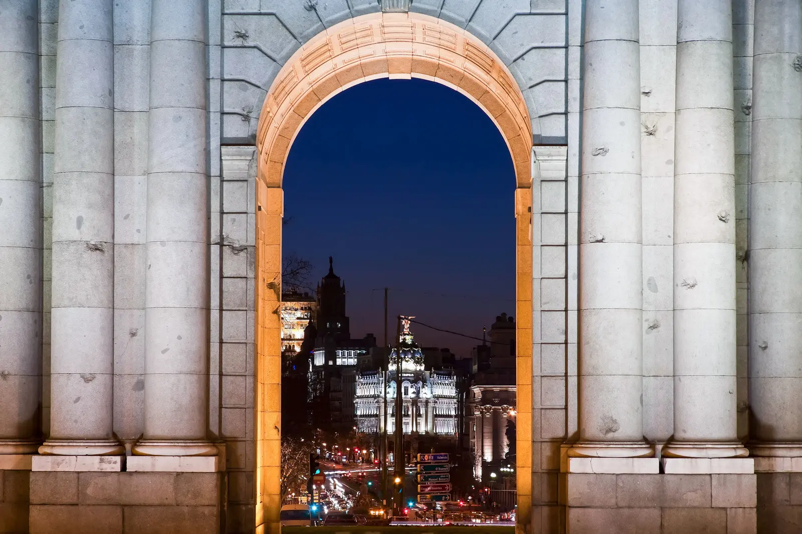 The central arch of the Puerta de Alcalá framing the illuminated Madrid skyline at night