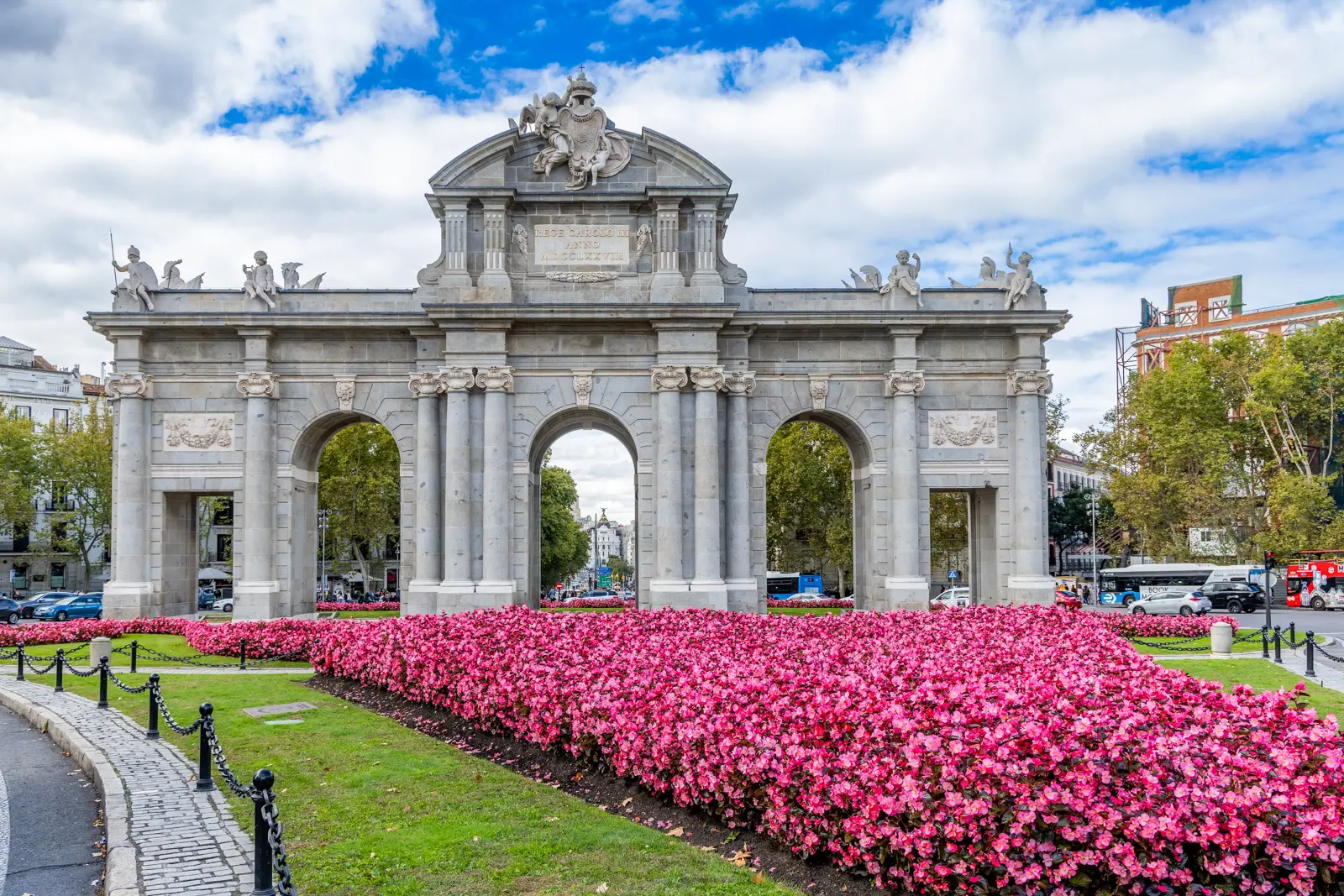 The Puerta de Alcalá surrounded by vibrant pink flowers in Plaza de la Independencia, Madrid