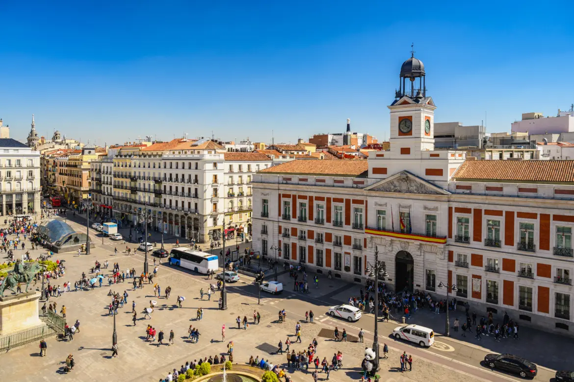 Aerial view of Puerta del Sol in Madrid showing the bustling square, the Casa de Correos clock tower, and the surrounding historic cityscape