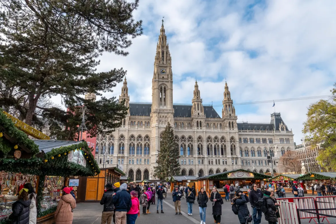 Daytime view of the Wiener Christkindlmarkt at Rathausplatz with wooden stalls, Christmas tree, and the neo-Gothic Vienna City Hall in the background, Vienna, Austria