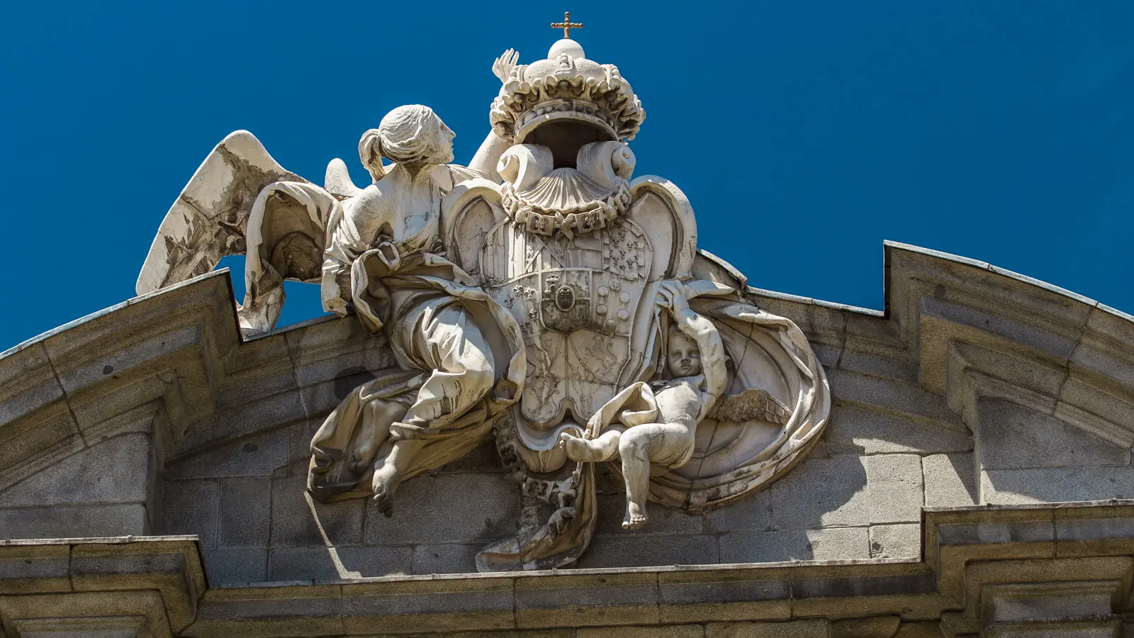 Close-up of the royal shield of Spain with angelic figures carved in white Colmenar stone atop the Puerta de Alcalá pediment