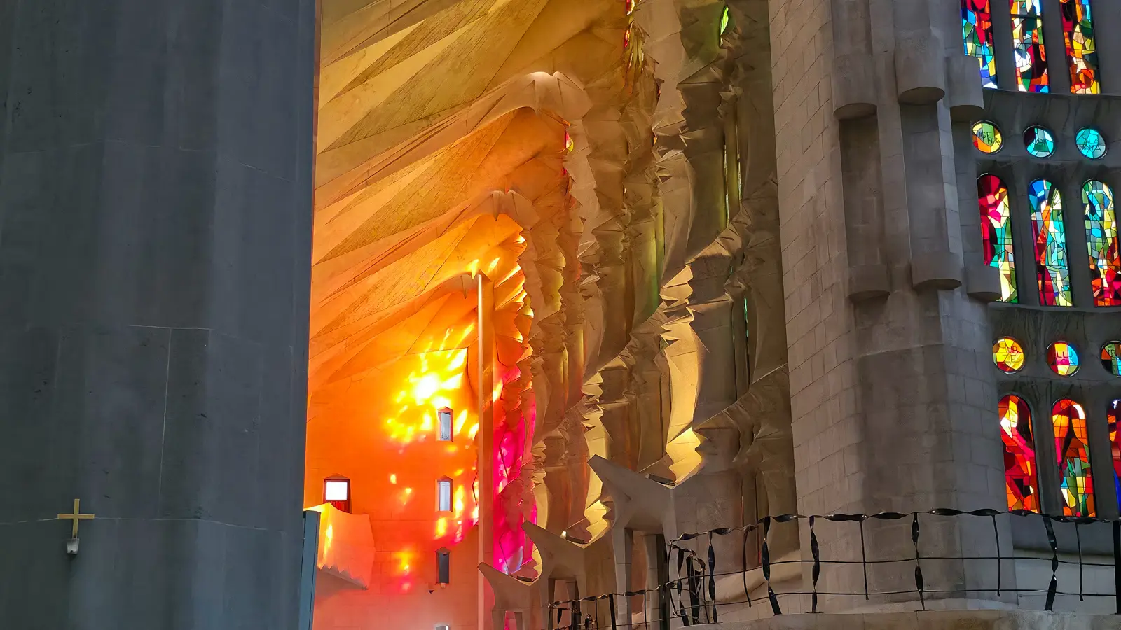 Inside the Sagrada Família with sunlight pouring through the west-facing stained glass windows, turning the forest-like nave into a kaleidoscope of amber, gold, and rose light