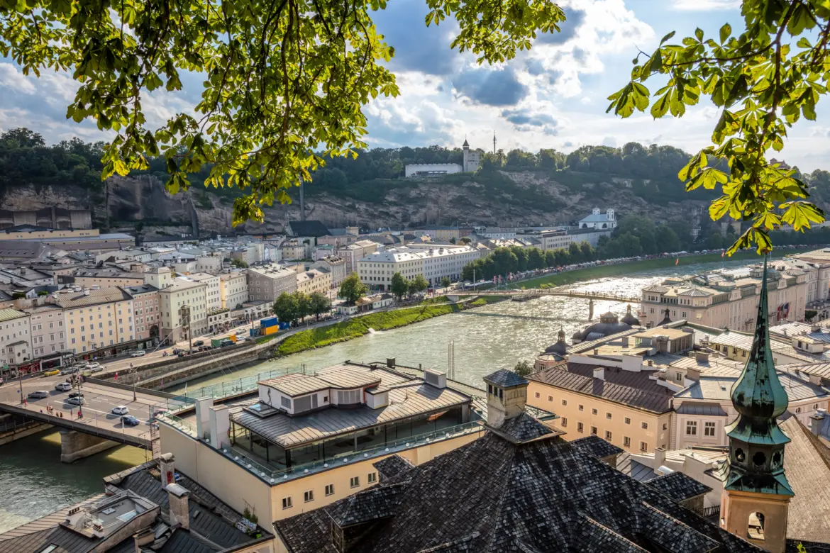 Elevated view of the Salzach river flowing between the Old Town and newer districts of Salzburg with framing chestnut foliage