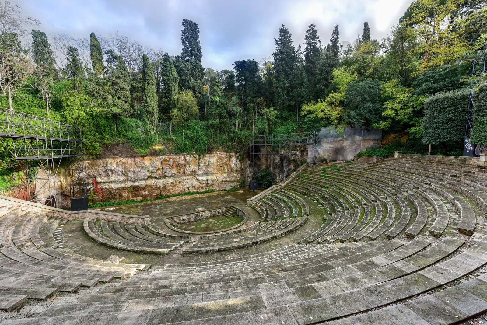 The Greek-style amphitheater at Jardins del Teatre Grec on Montjuïc in Barcelona, with stone tiers carved into the hillside and cypress trees framing the stage