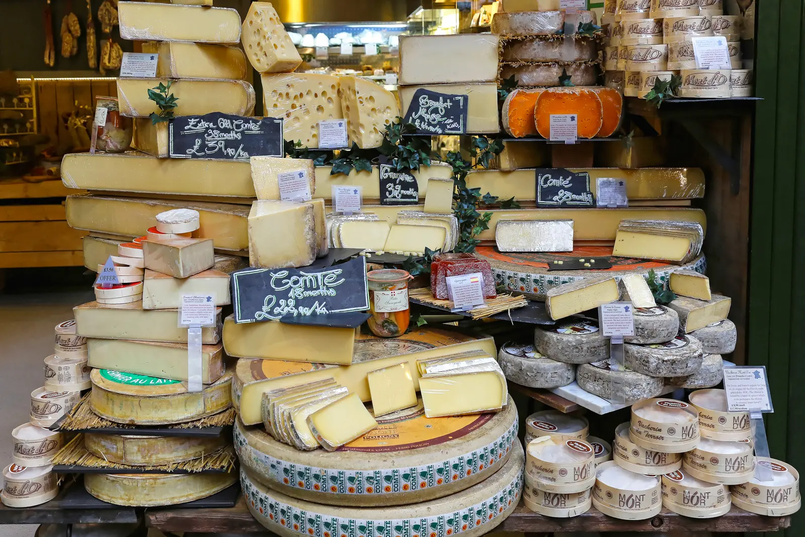 A pyramid display of French and Alpine cheeses at Borough Market including wheels of Comté at different ages, Mont d'Or in spruce-bark boxes, Beaufort, and assorted hard mountain cheeses