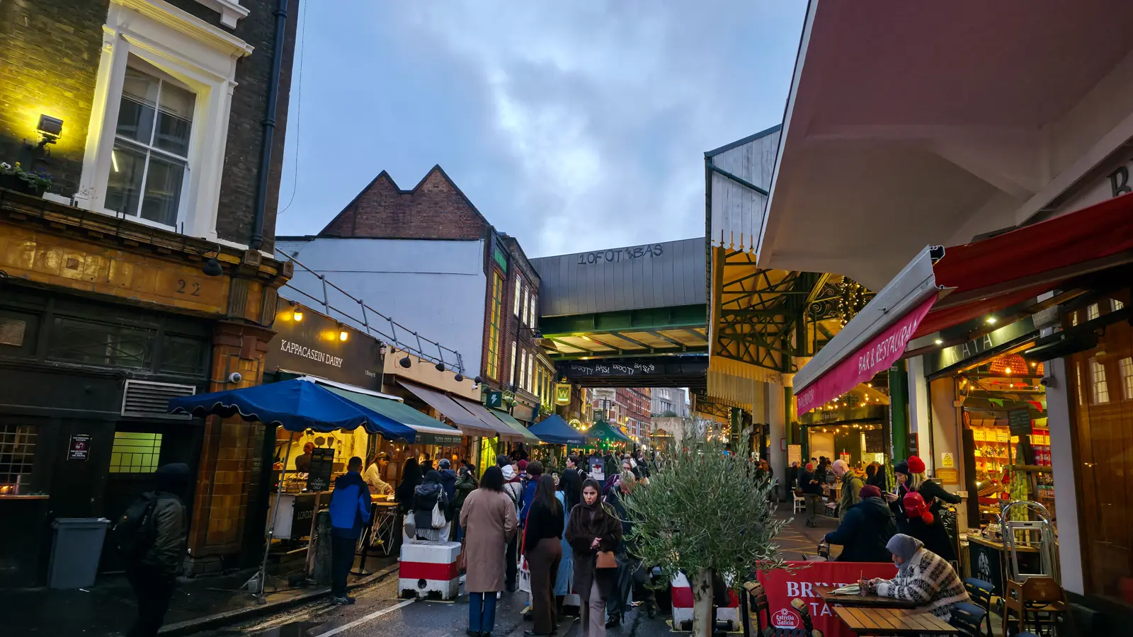 The Stoney Street outdoor section of Borough Market with the Kappacasein Dairy queue on the left, the elevated railway viaduct in the centre background, and the red Brindisa Tapas awning visible on the right