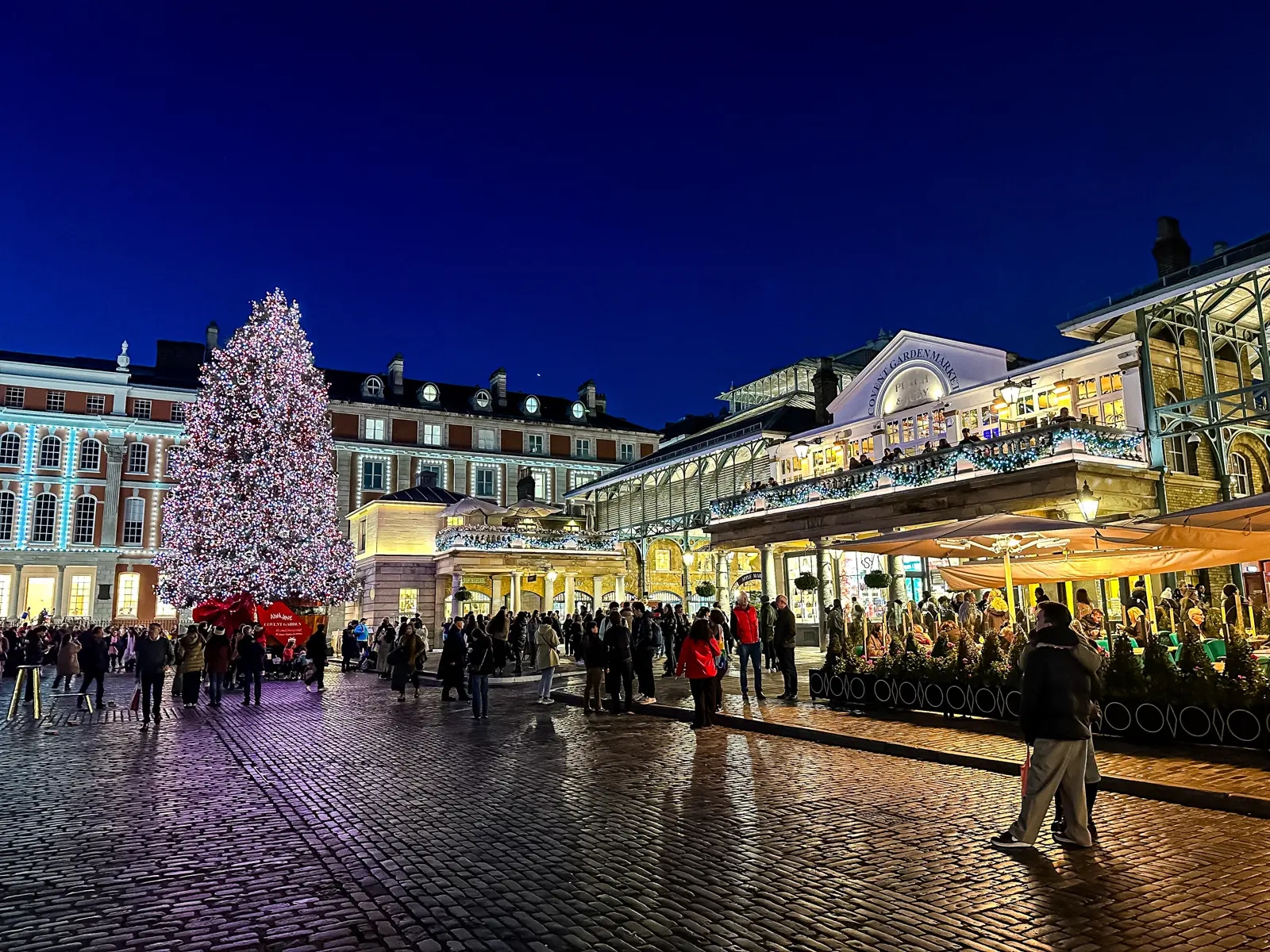 The illuminated Market Building of Covent Garden at night in London, decorated for Christmas and New Year with festive lights reflecting across the wet cobblestone streets