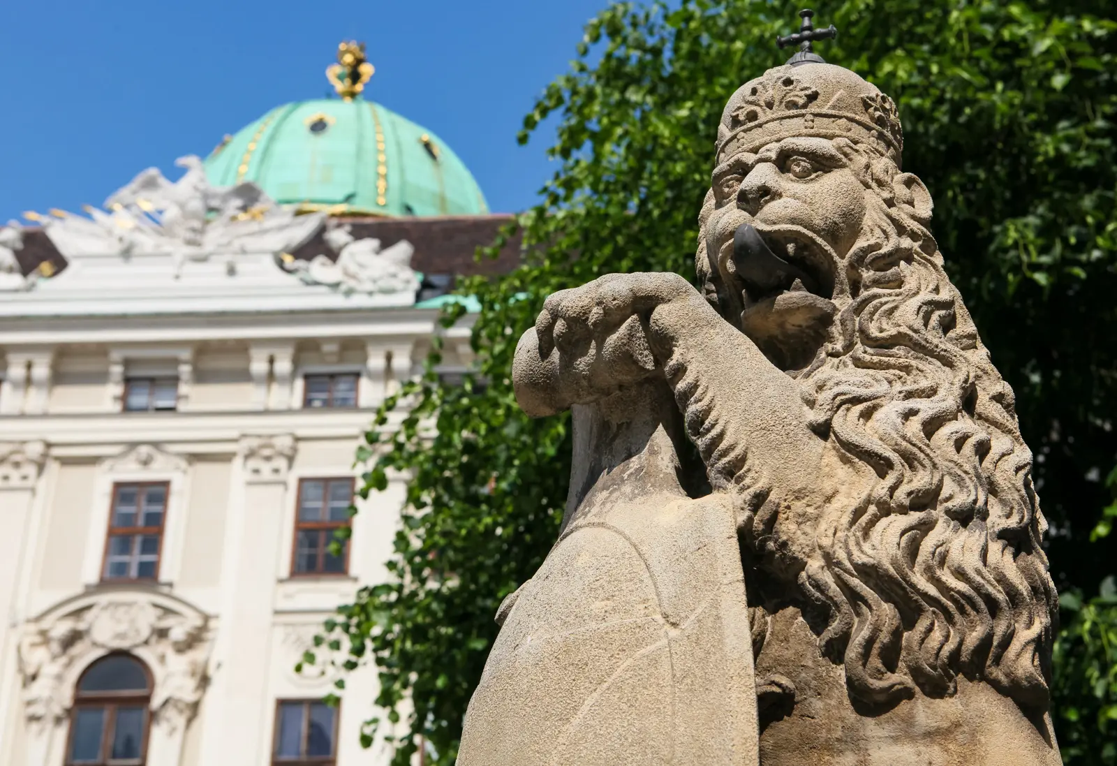 Stone lion statue wearing a crown and gripping a shield at Hofburg Palace in Vienna, evoking the ancestral Habsburg coat of arms