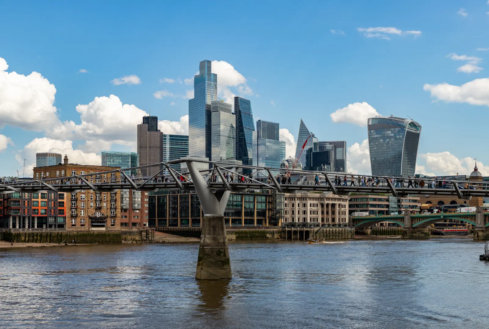 View of Millennium Bridge crossing the River Thames in London, with the modern financial district skyline rising in the background