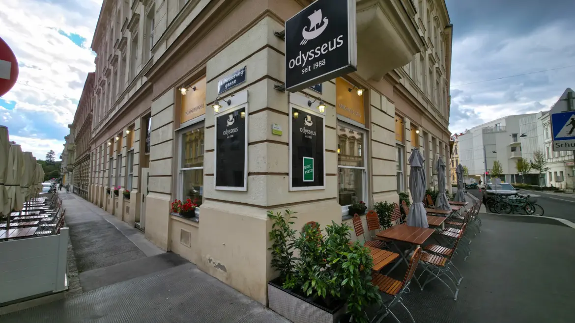 Corner exterior of Odysseus Greek restaurant in Vienna with sidewalk terrace tables and the trireme logo sign