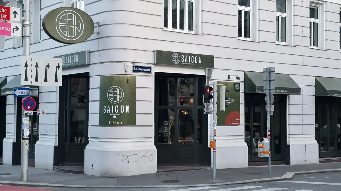 Exterior of Saigon Vietnamese restaurant on the corner of Getreidemarkt and Lehárgasse in Vienna's 6th district, with olive-green storefront and circular Saigon signage