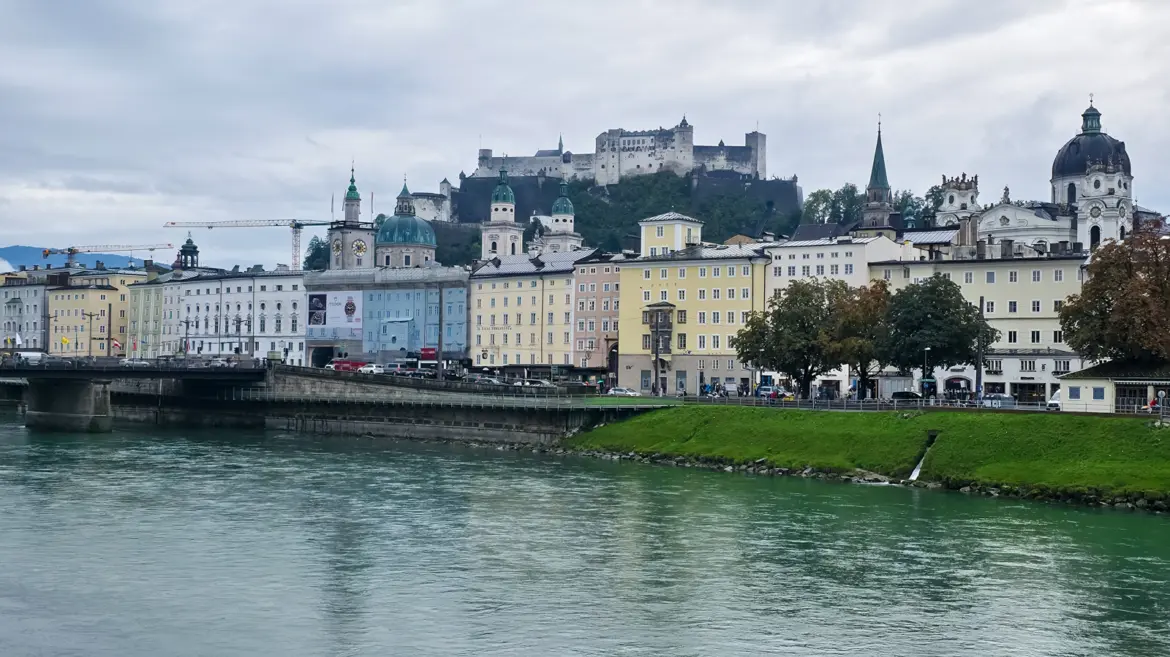 Salzburg Old Town skyline viewed from across the Salzach River under overcast sky with Hohensalzburg Fortress crowning the hill