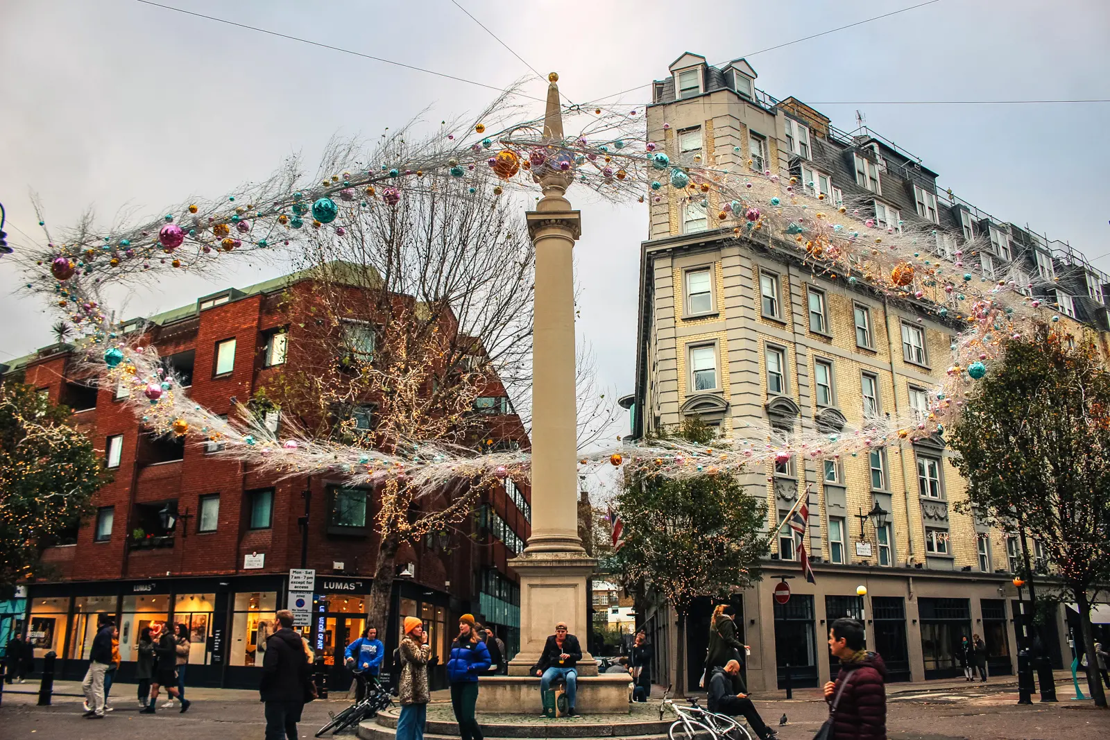 The historic Seven Dials junction near Covent Garden viewed from Monmouth Street in London, featuring festive holiday decorations surrounding the iconic central sundial monument