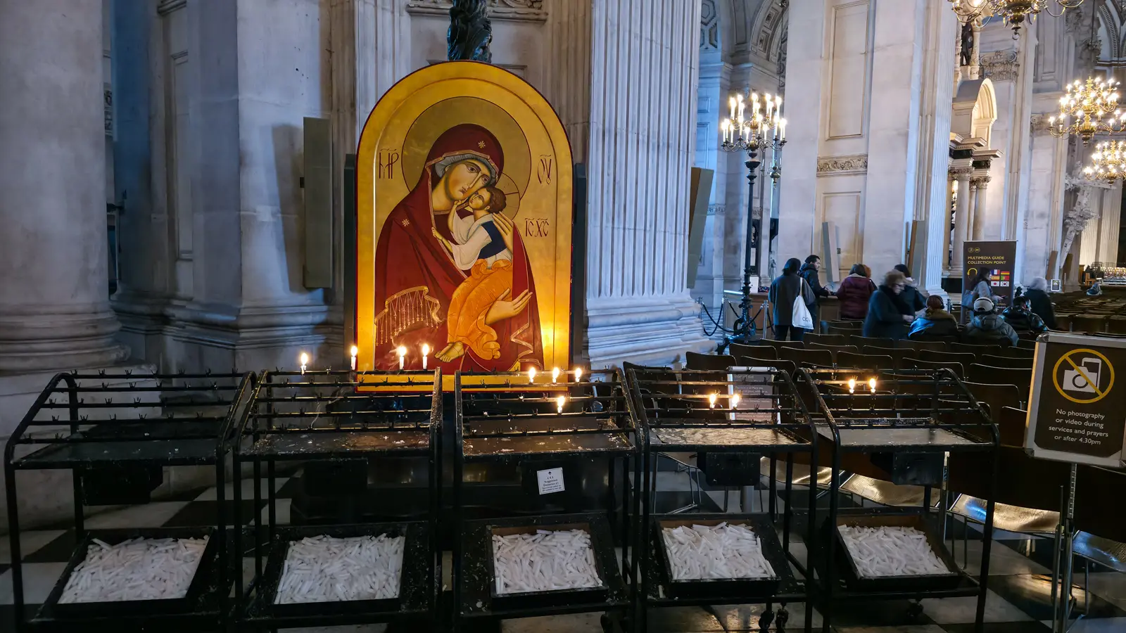 Byzantine-style icon of the Virgin Mary holding the infant Christ cheek-to-cheek in the nave of St Paul's Cathedral, with rows of small votive candles burning on tiered iron stands in front