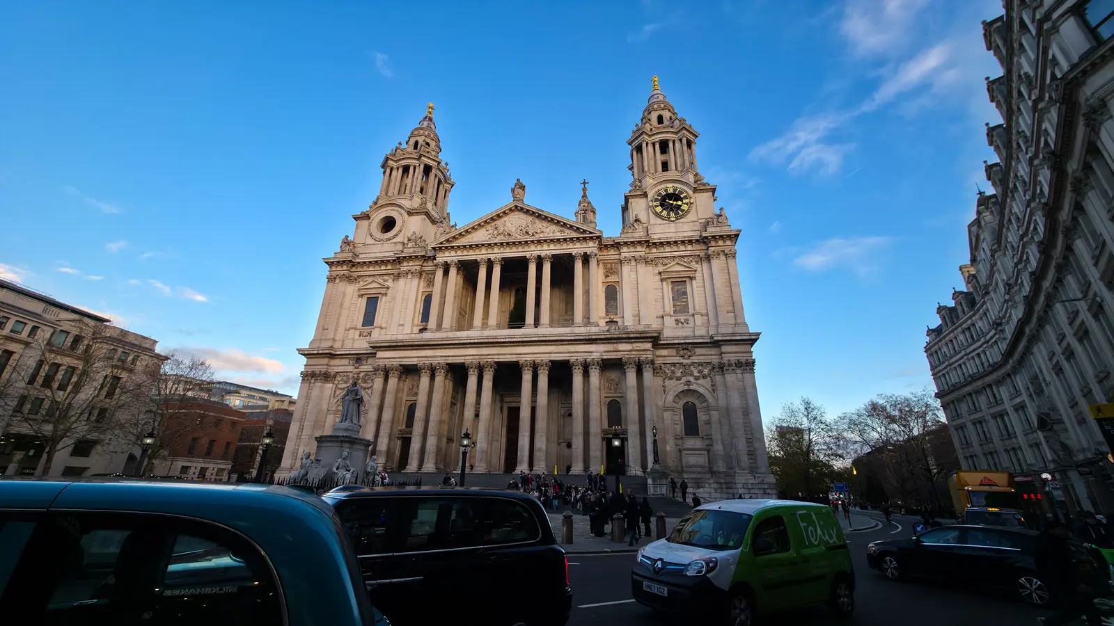 The west front of St Paul's Cathedral in late-afternoon December sunlight, with its twin Baroque towers, central pediment carved with the Conversion of St Paul, and the statue of Queen Anne in front