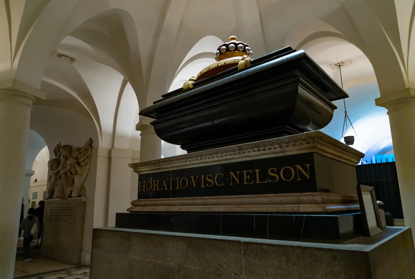 Close-up side view of Nelson's polished black marble sarcophagus in the crypt of St Paul's Cathedral, showing the gilt HORATIO·VISC·NELSON inscription and the viscount's coronet with ermine band on top