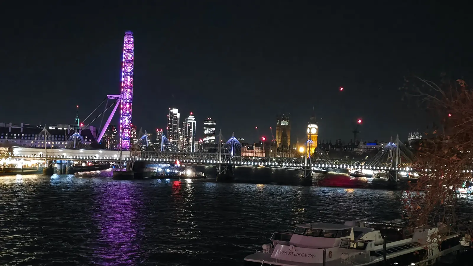Night view of the River Thames in London featuring the illuminated London Eye and Big Ben reflected across the water