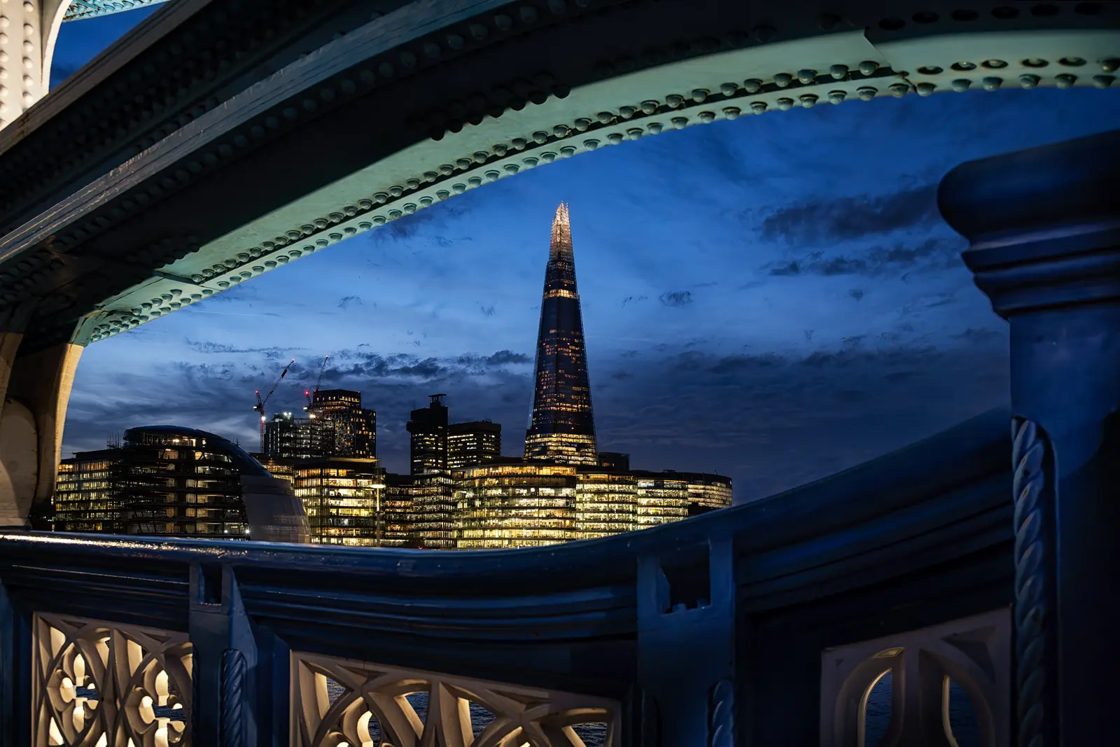 Night view of The Shard and the More London riverside district framed through the structure of Tower Bridge in London