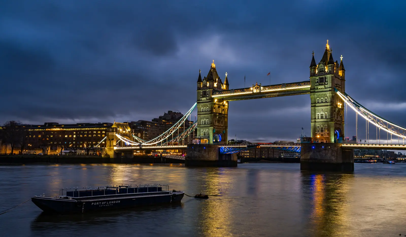 Night view of Tower Bridge illuminated above the River Thames in London, where reflections and Victorian architecture create one of the city's most atmospheric nighttime scenes