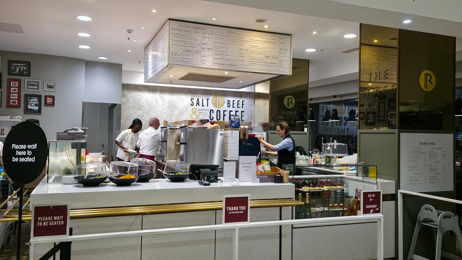 The Salt Beef & Coffee counter at the Brass Rail in Selfridges, with the menu board above and staff preparing food behind it