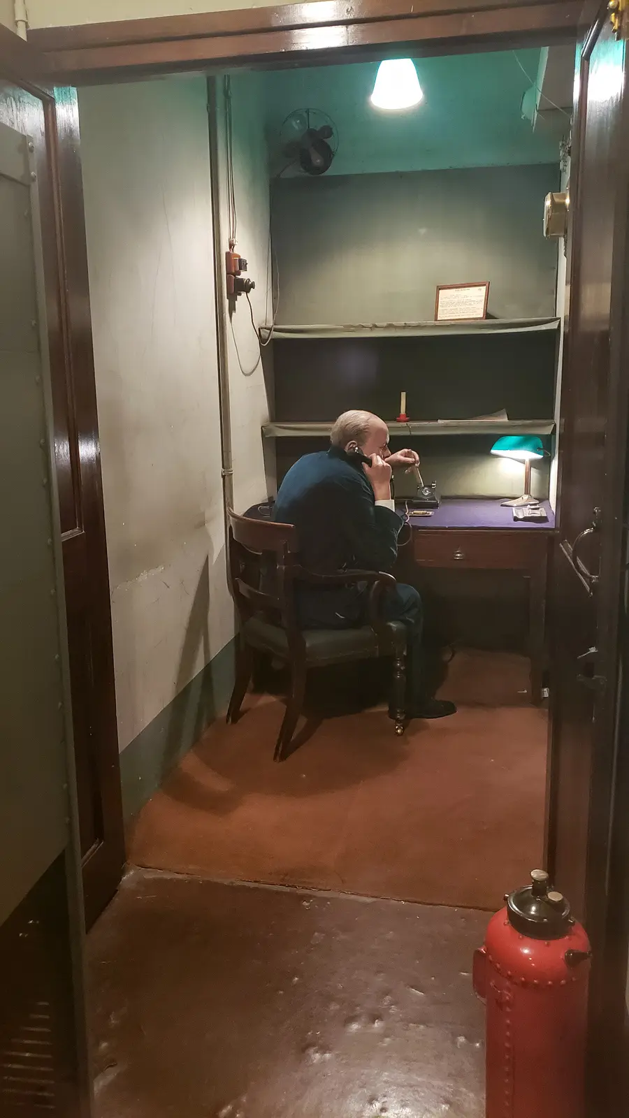 A figure of Winston Churchill at a desk on the telephone in a small room at the Churchill War Rooms, London