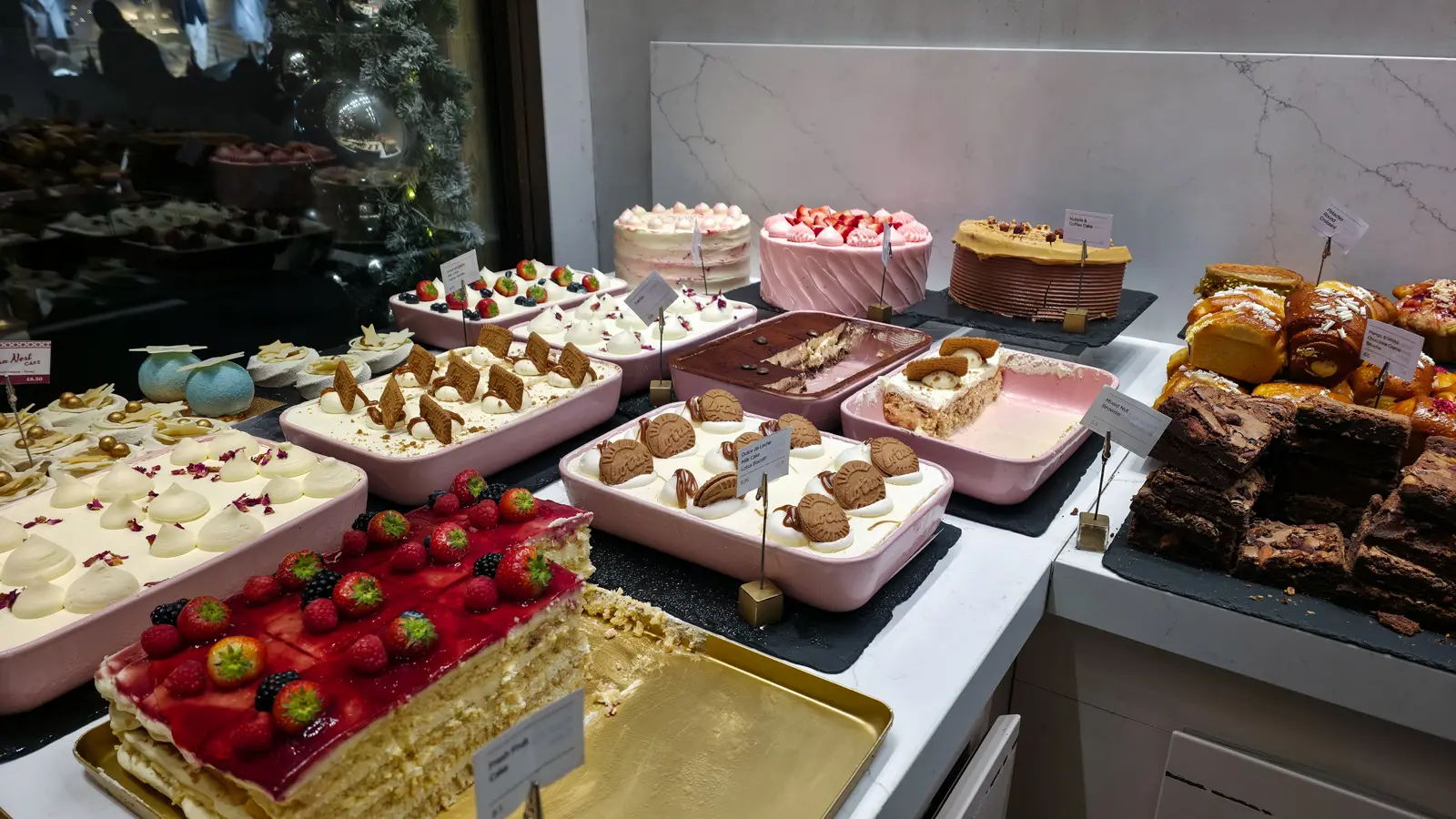EL&N London cake counter with Lotus Biscoff tray bakes, a berry-topped fresh fruit cake and mixed nut brownies