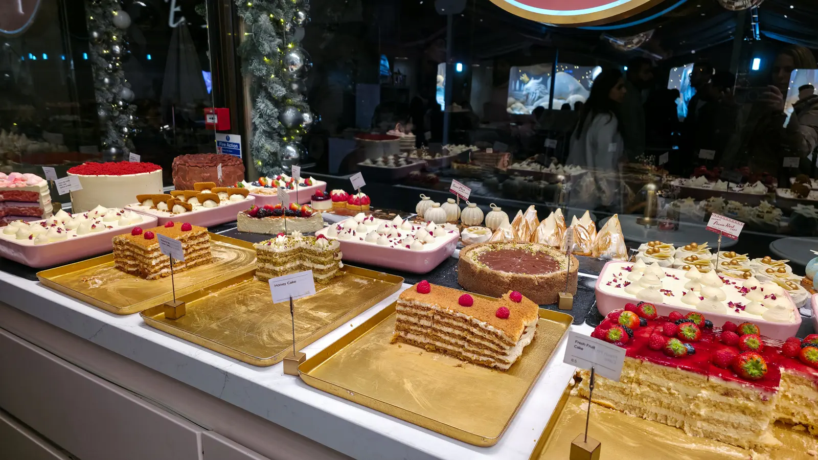 Sliced honey cake, meringue-topped cakes and a fresh fruit cake on gold trays at EL&N London Knightsbridge